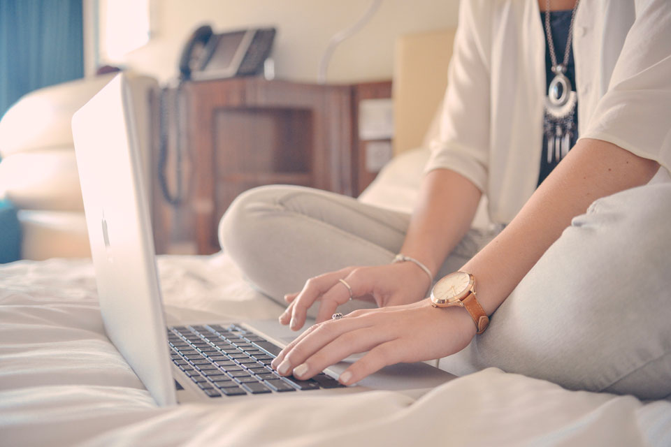 Ateliers d'écriture : une femme tape à l'ordinateur sur son lit